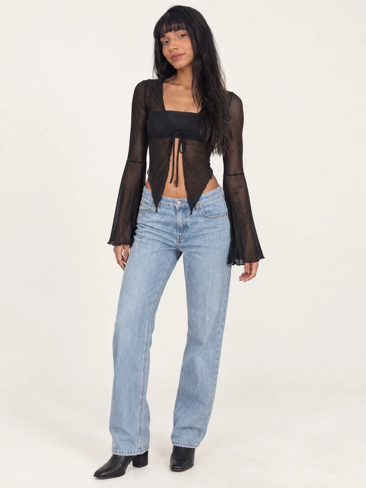 Adriely de frente com blusa de tule preta com amarração e mangas sino, jeans claro