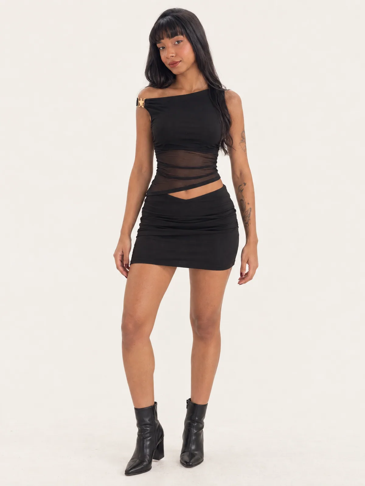 Adriely de frente com conjunto preto de top assimétrico com fecho dourado e minissaia franzida