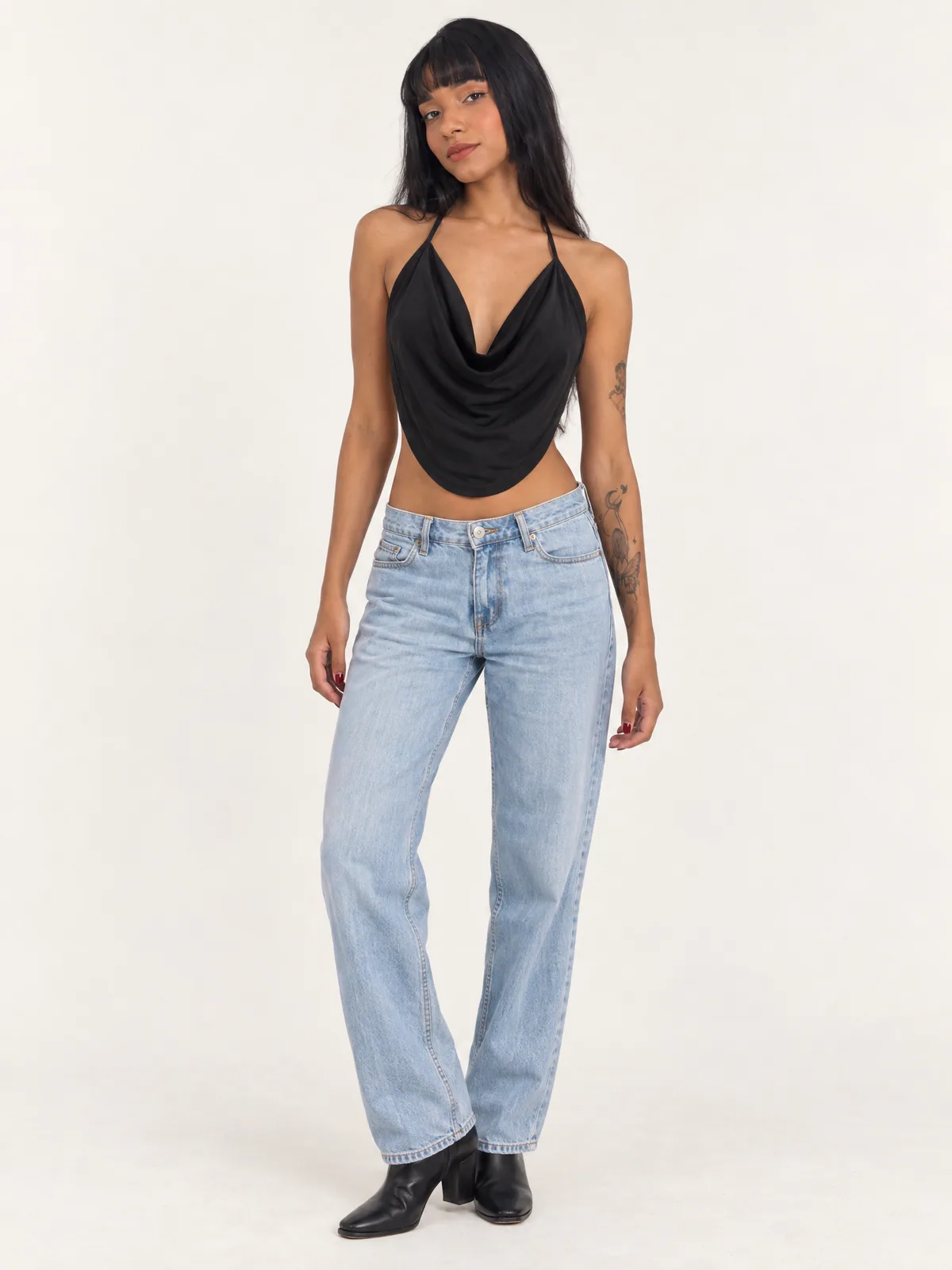 Modelo de frente com top frente única preto de decote degagê e barra arredondada, calça jeans clara